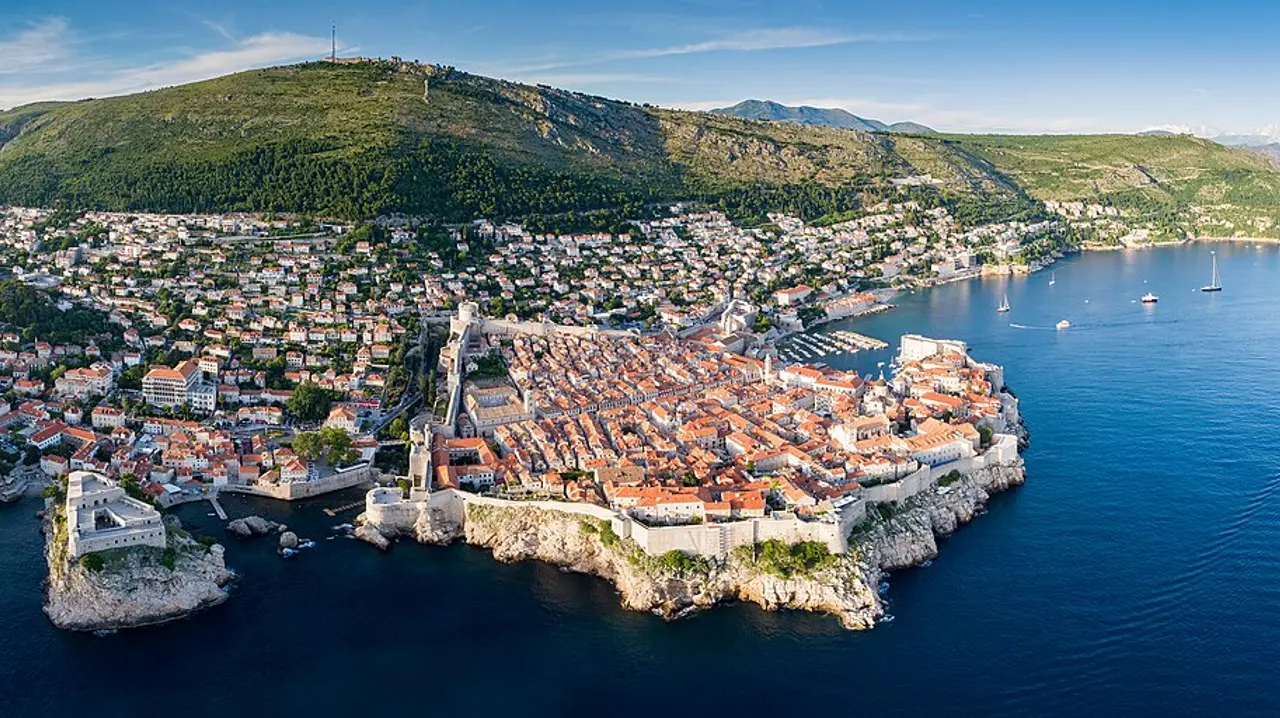 Aerial panorama of the walled Old Town of Dubrovnik, the full ring of stone walls wrapping the terracotta rooftops above the sea