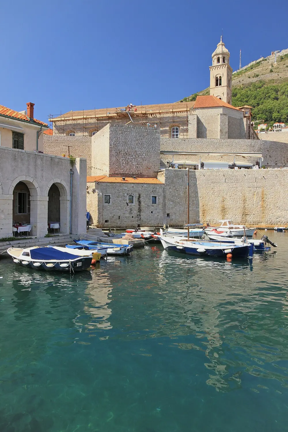 Dubrovnik's Old Port with small fishing boats below the city walls and the Dominican monastery bell tower behind