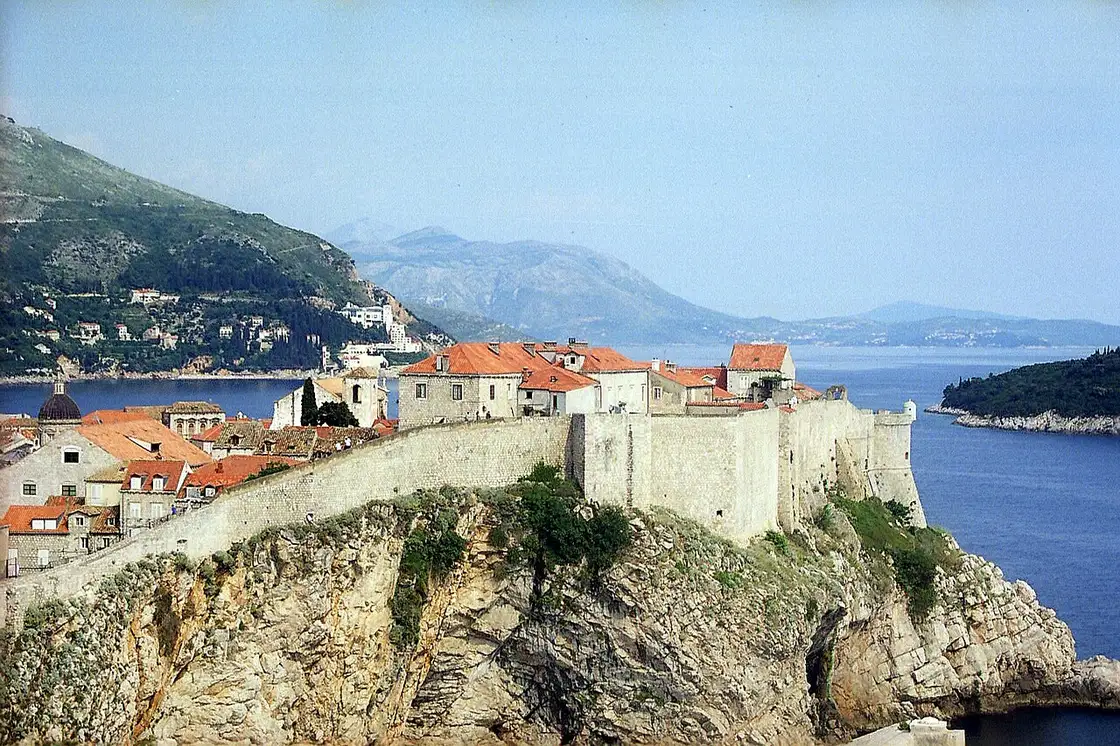 The Dubrovnik city walls running along the clifftop above the sea toward Fort Bokar, with the island of Lokrum behind