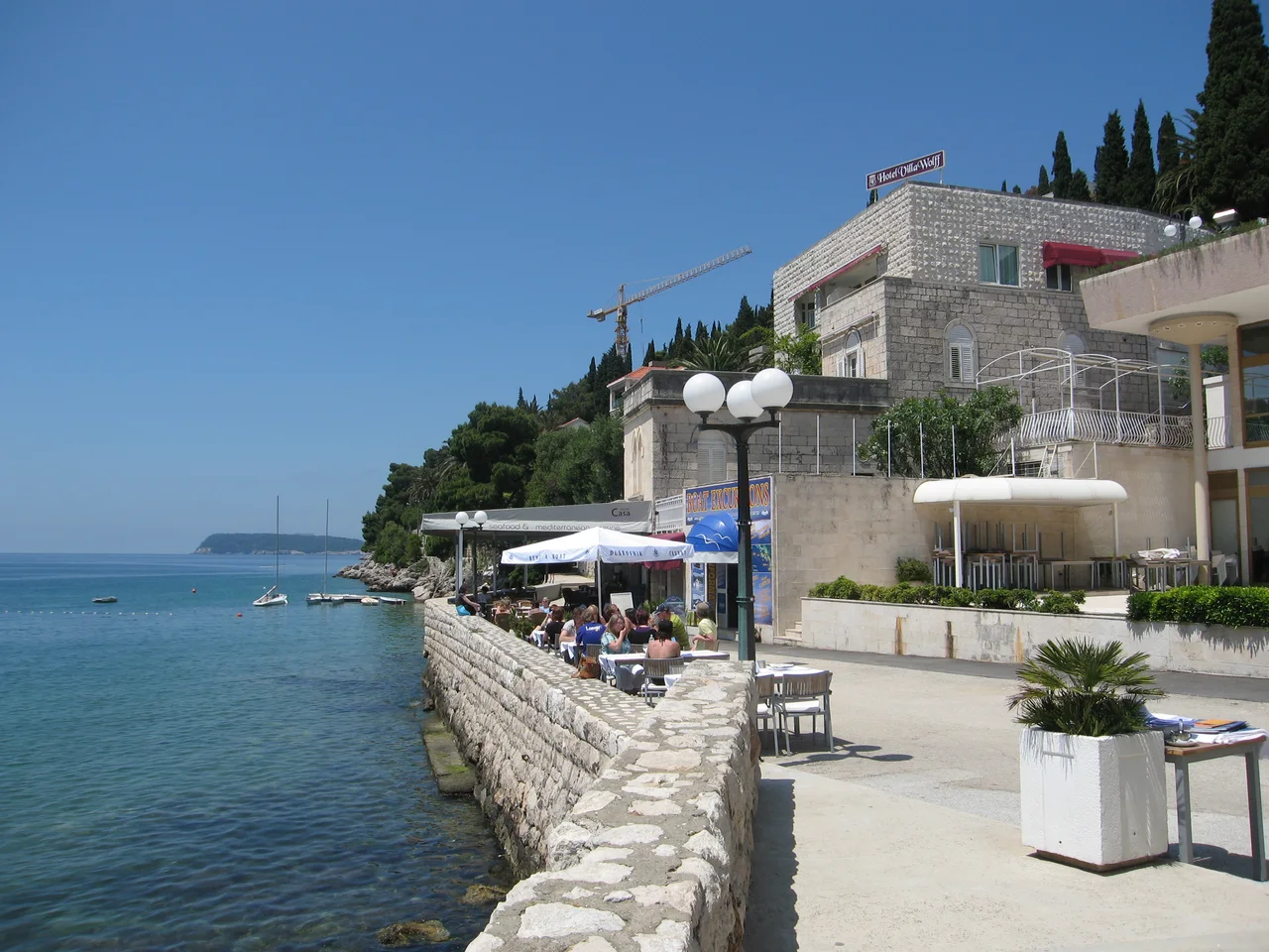 The seafront promenade in Lapad, Dubrovnik, with restaurant terraces along a stone wall above clear water