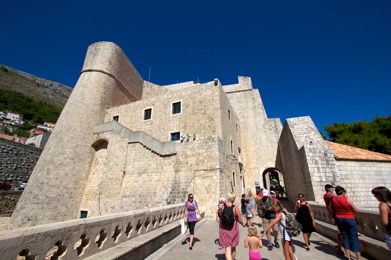 The massive stone walls and round bastion of Fort Revelin in Dubrovnik, with visitors crossing the stone bridge to its gate