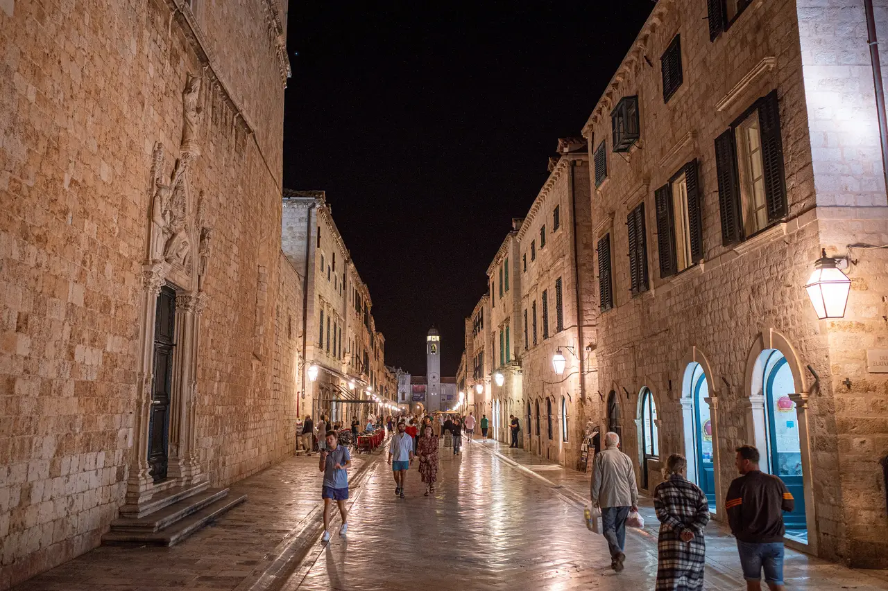 The Stradun, Dubrovnik's polished limestone main street, lit by lanterns at night with people walking towards the bell tower