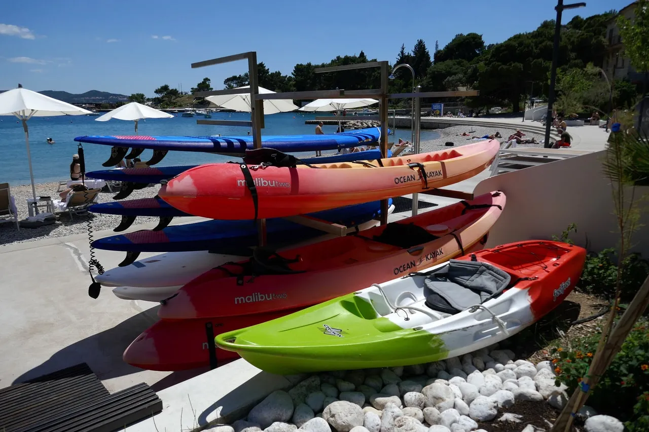 Red and green plastic sea kayaks and paddleboards racked on a pebble-beach promenade