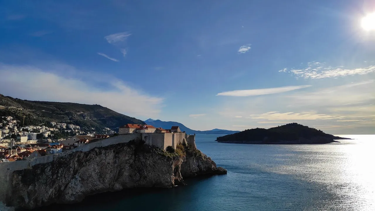 The cliff under Fort Lovrijenac with the city wall above it and the dark island of Lokrum on the horizon