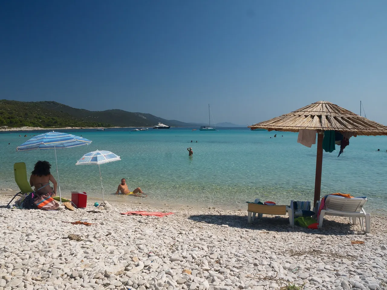 People swimming in the clear turquoise water of Sakarun beach with white sand and pines