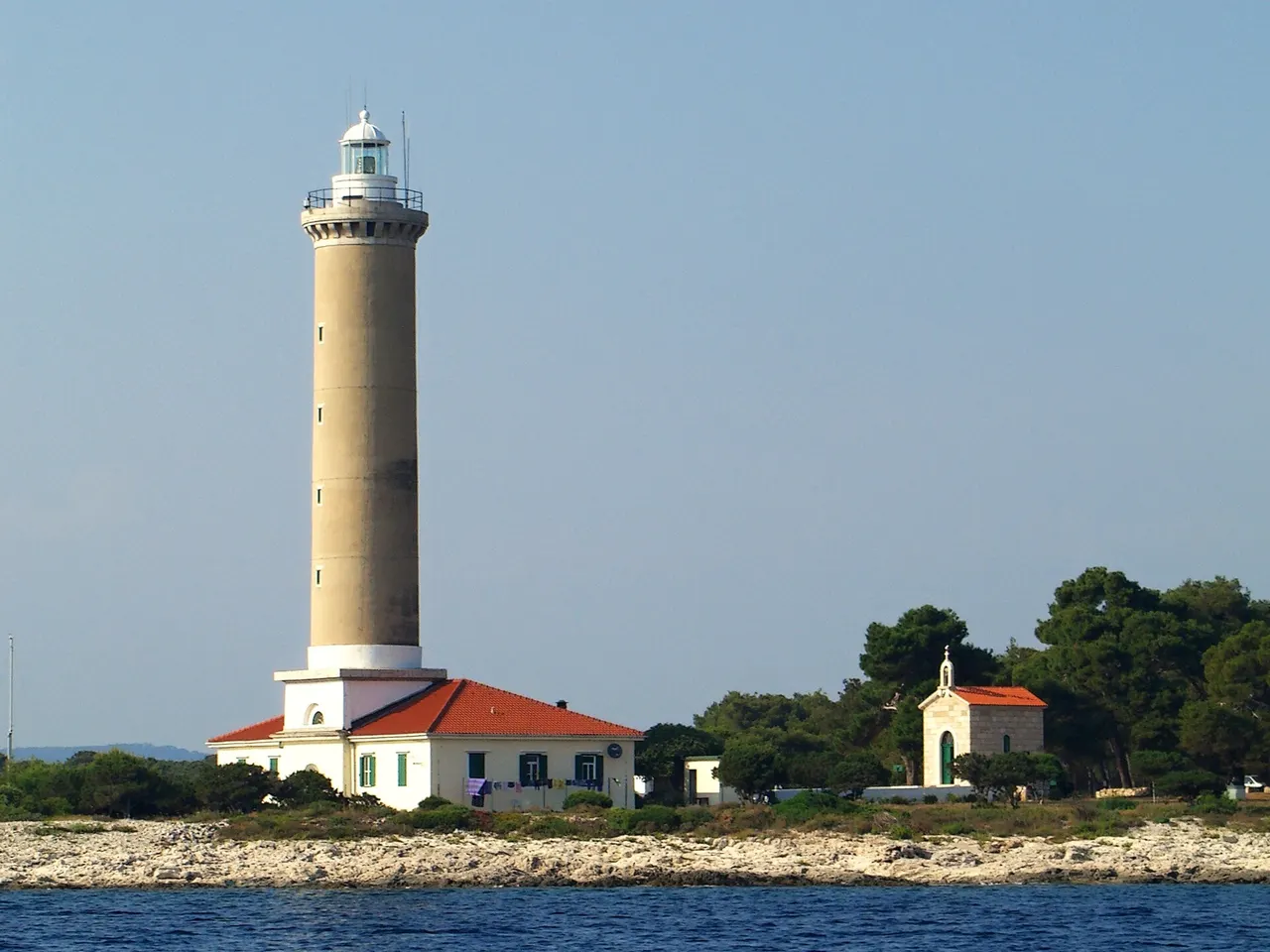 Close view of the cylindrical white tower and keeper buildings at Veli Rat lighthouse