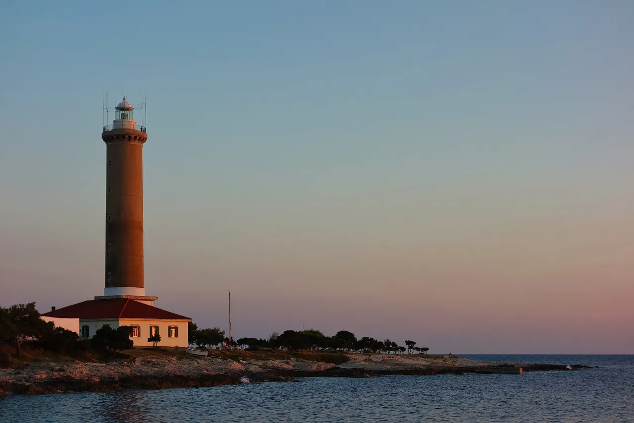 The white stone tower of Veli Rat lighthouse rising above pines on the northwest tip of Dugi Otok