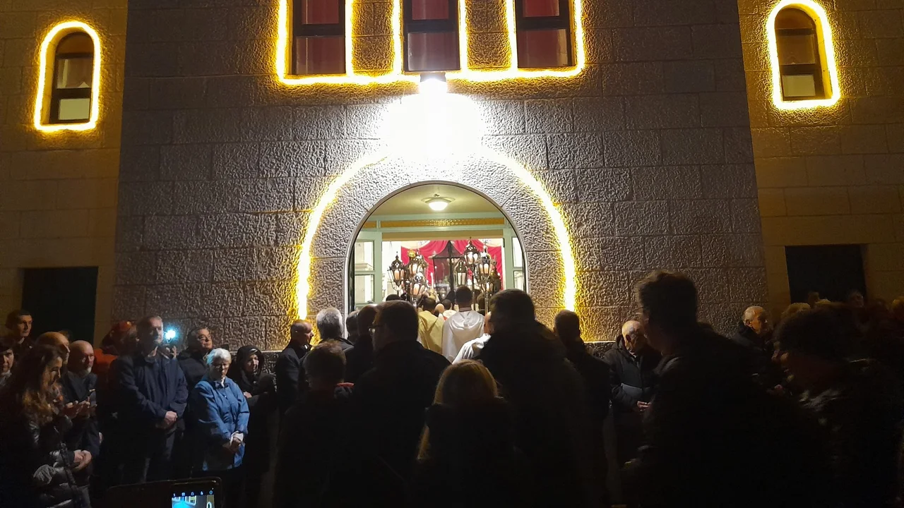 A crowd gathers at the lit doorway of a village church on Hvar at night as processional lanterns and a cross are carried out for Za križen