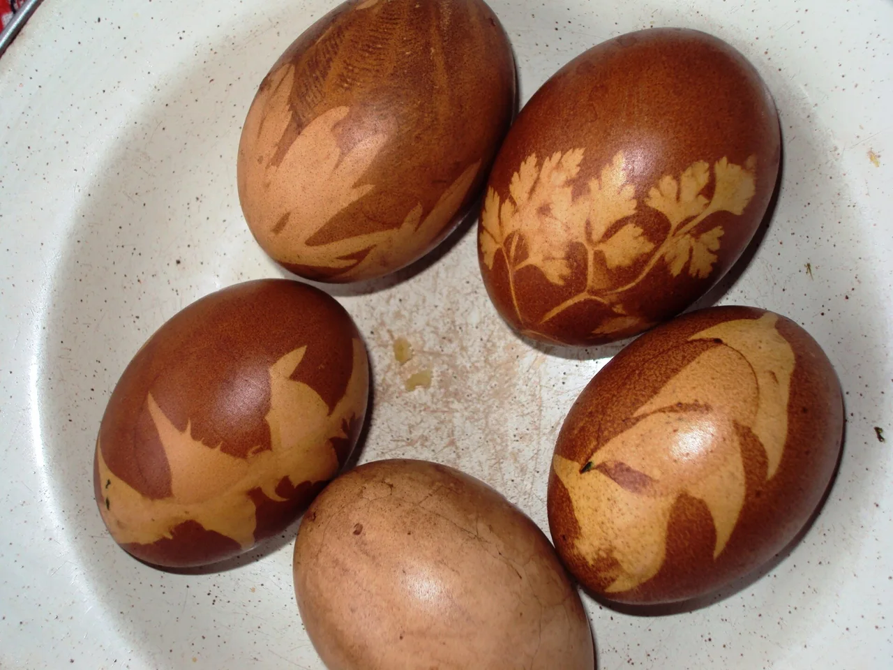 Five boiled eggs dyed brown with pale leaf prints on the shell, lying in a white bowl
