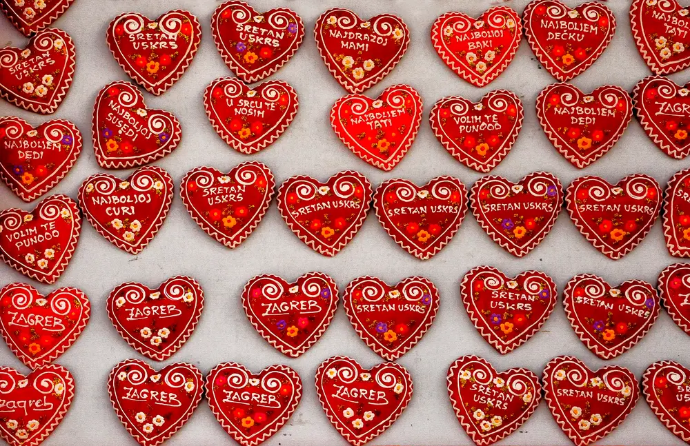 Rows of decorated red hearts with white icing swirls and small flowers, lettered Sretan Uskrs, Zagreb and short messages to relatives