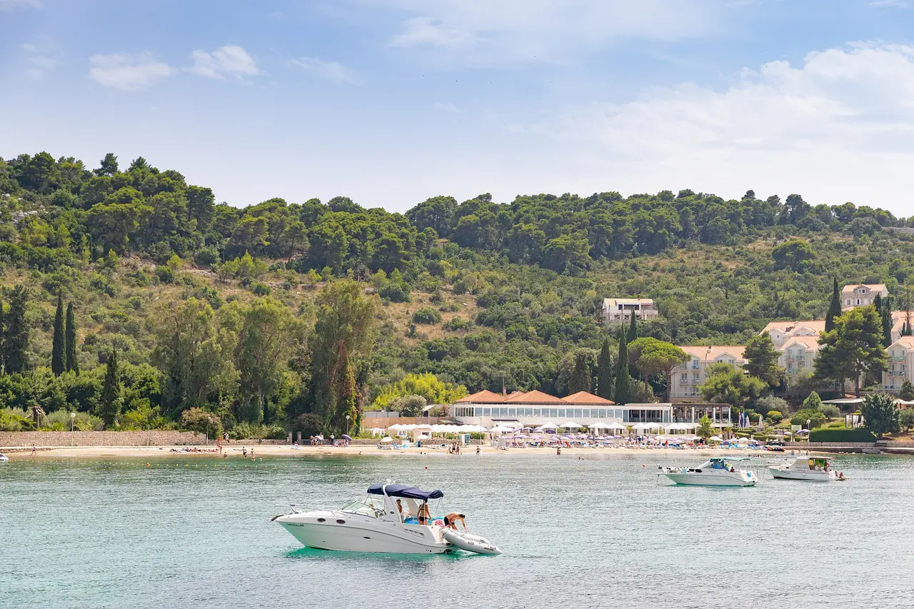 Donje Čelo bay on Koločep with a sandy crescent, rows of white umbrellas and motorboats at anchor