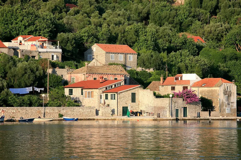 Stone houses with terracotta roofs and bougainvillea on a quay on Šipan, small boats moored in front