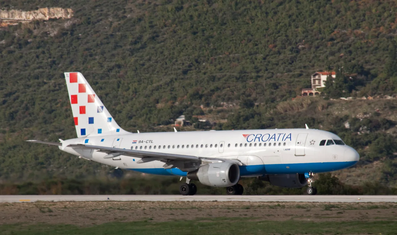 A white Croatia Airlines Airbus A319 with the red-and-white chequerboard tail on the runway at Dubrovnik, a wooded hill behind