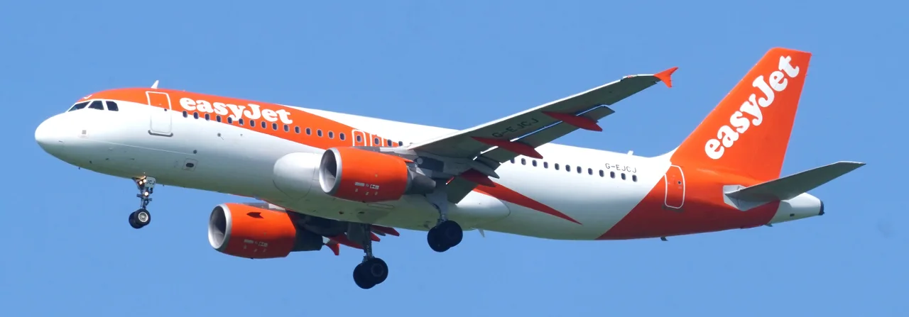 An easyJet Airbus A320 in orange and white livery on approach to Gatwick, landing gear down, against a clear blue sky
