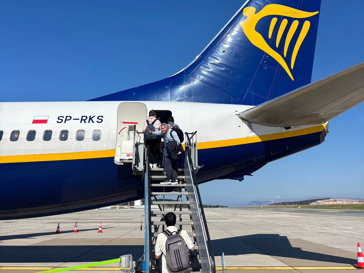 Passengers climbing the boarding stairs of a Ryanair-liveried Boeing 737 on the apron at Dubrovnik, the blue tail with the yellow harp behind them
