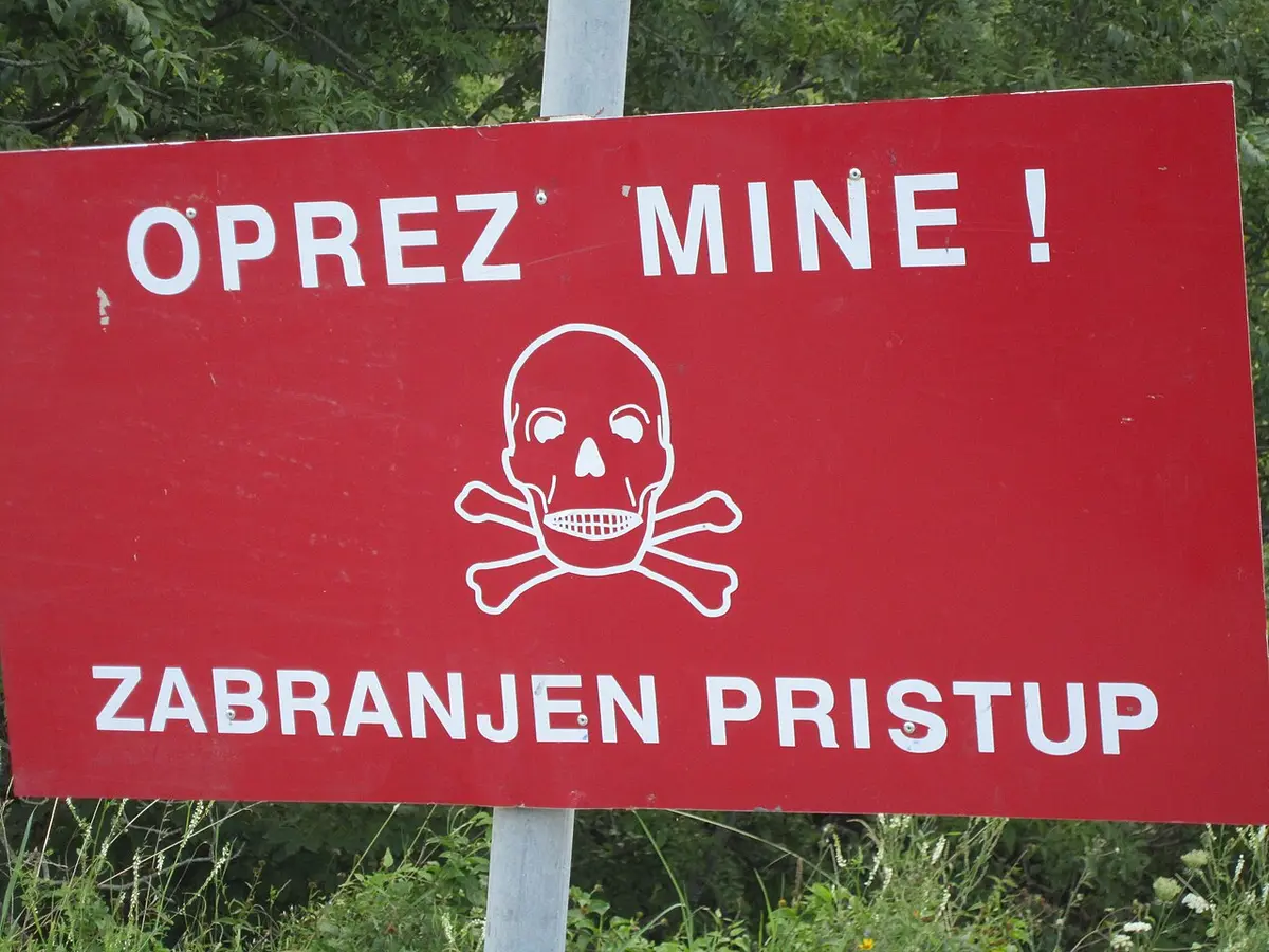 A red warning sign reading Ne prilazite - mine marking a former minefield beside a field in rural Croatia