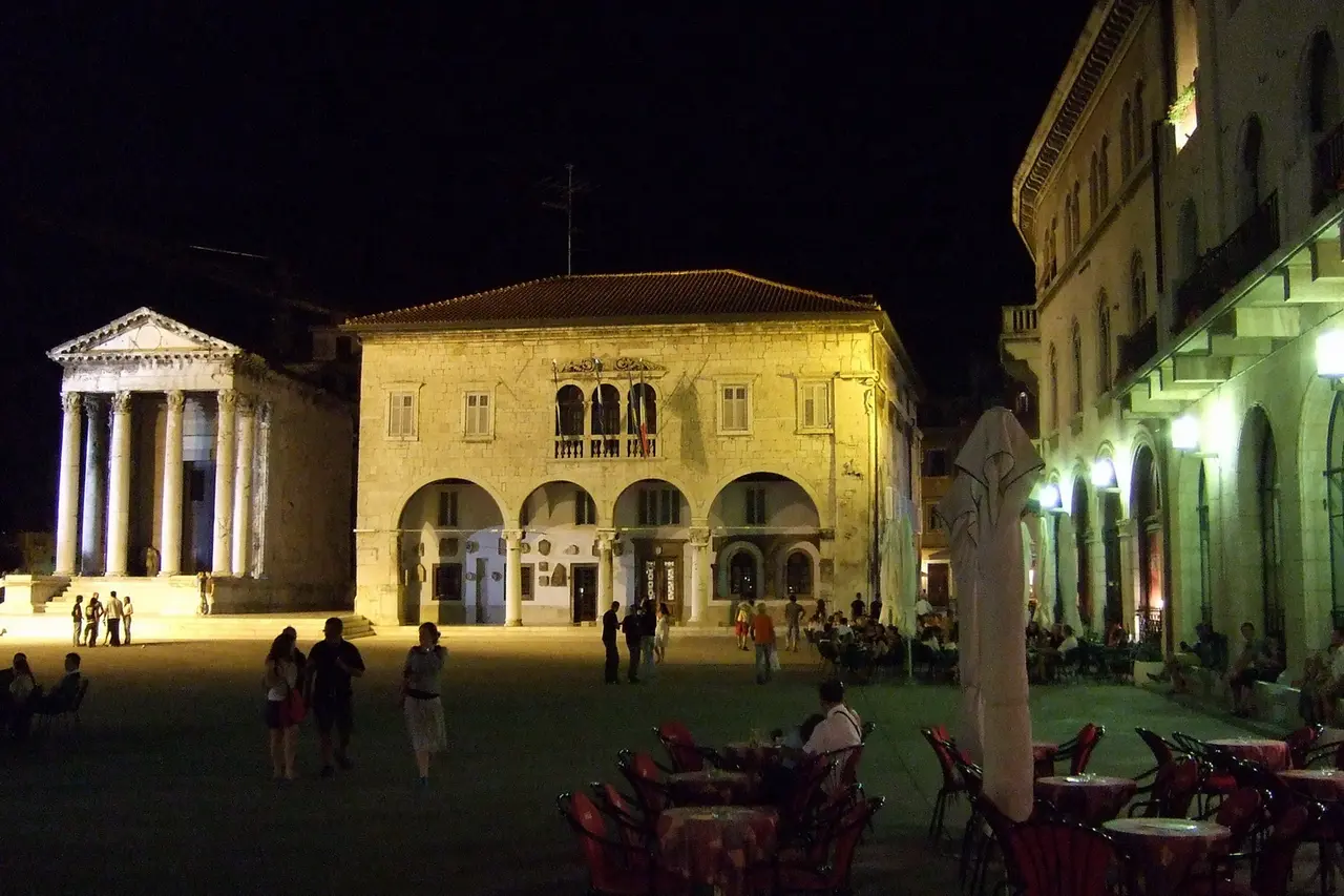 The Forum square in Pula lit up at night, with the columned Temple of Augustus on the left and the old town hall in the centre