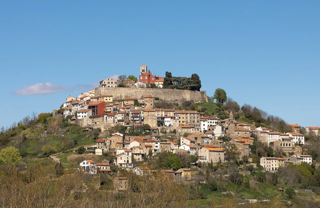 The walled hilltop town of Motovun crowning a green vineyard hill under a clear blue sky in inland Istria