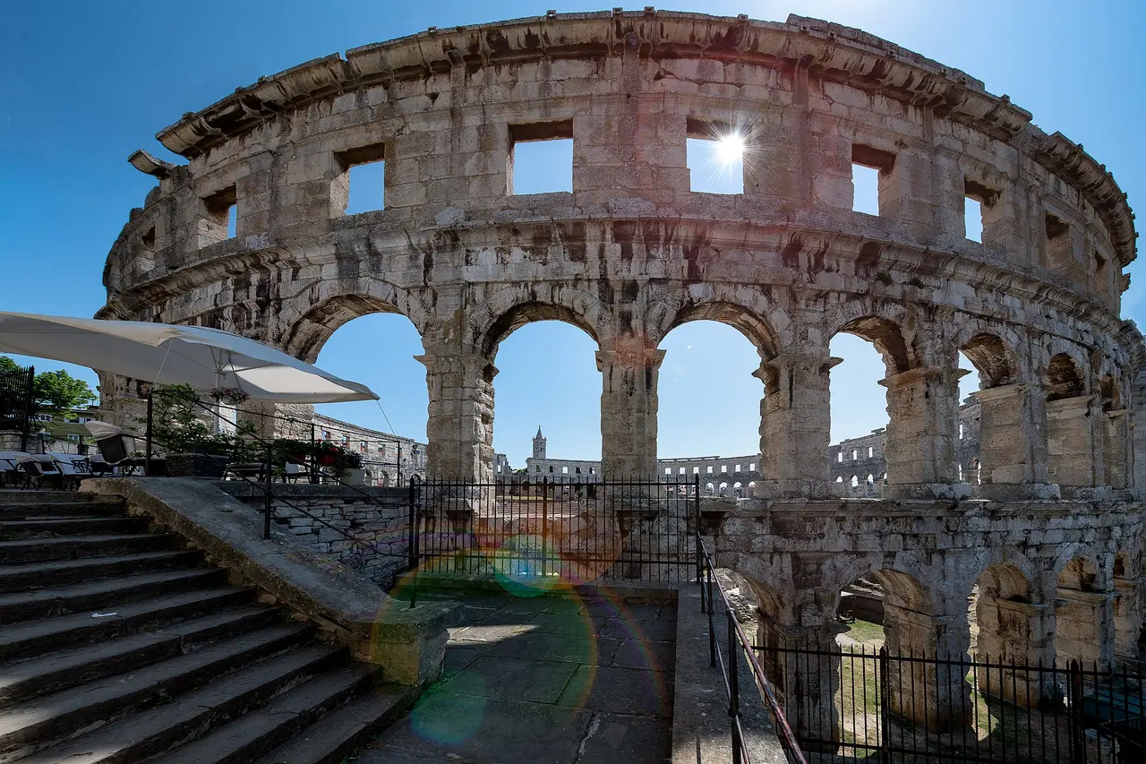 The arched outer wall of the Roman Arena in Pula seen from inside, with sunlight through the upper windows