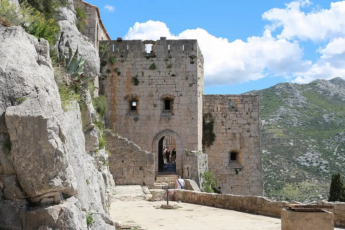 Long stone curtain wall of Klis Fortress running along the ridge with dry hills behind