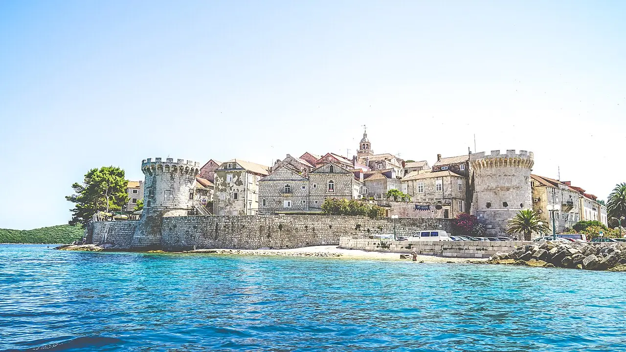The old town of Korčula seen from the water, a wall of stone houses and a tall church tower rising straight from the sea