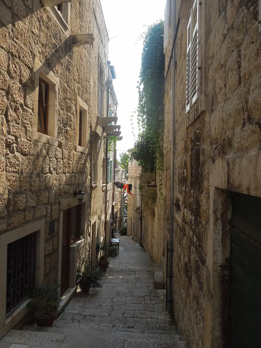 A narrow stone street in Korčula old town rising in steps between tall shuttered houses