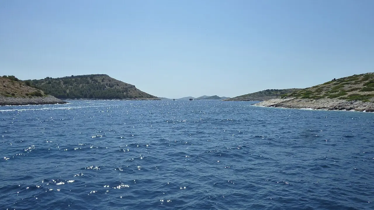 View from a boat threading a blue channel between the bare, low islands of the Kornati archipelago