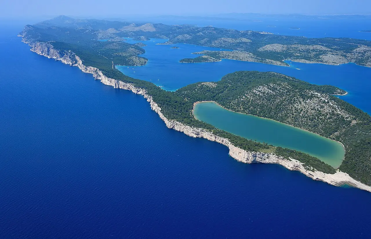 Aerial view of the Telascica cliffs dropping to the sea on Dugi Otok with the green Mir salt lake behind and the Kornati islands beyond