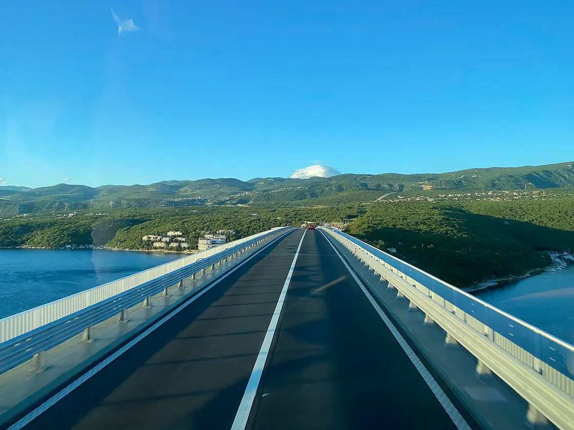 The carriageway of the Krk Bridge with the island and green hills ahead