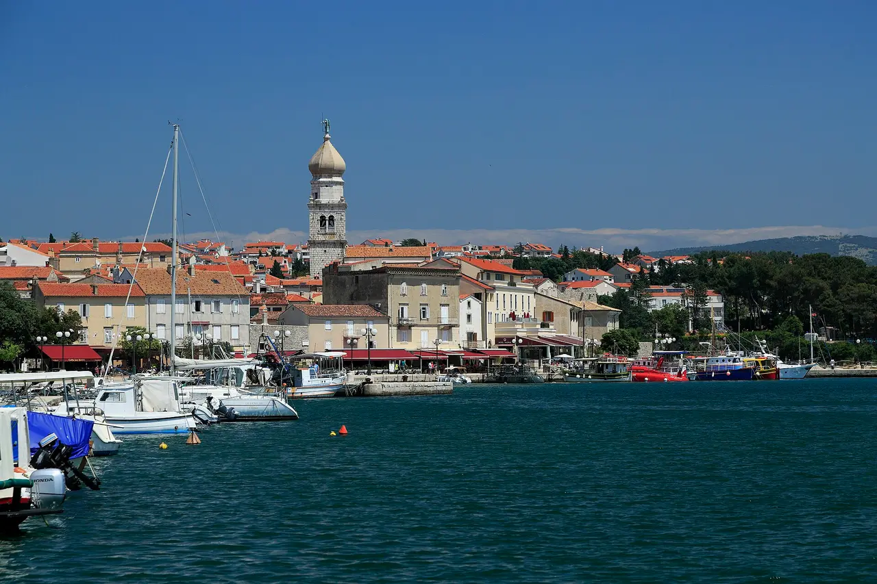 The waterfront of Krk town with fishing boats and the cathedral bell tower behind