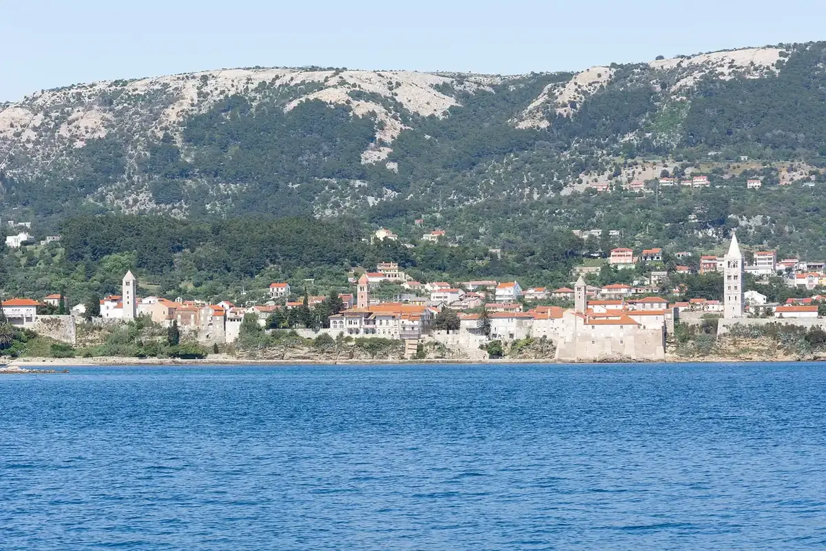The four bell towers of Rab old town rising above stone roofs and the harbour