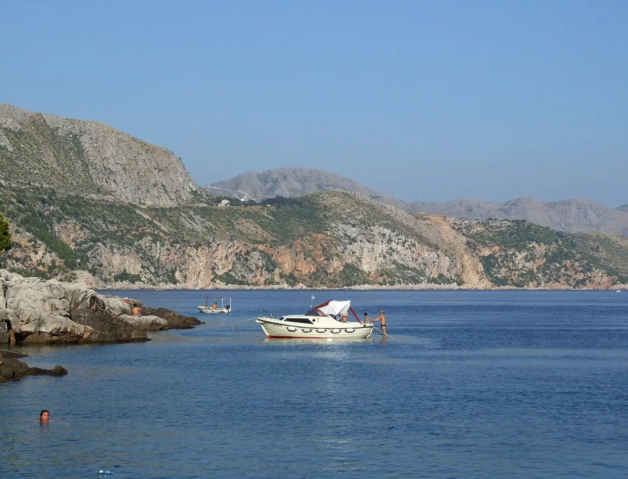 Swimmers and small boats in a rocky cove on Lokrum with the mainland cliffs behind