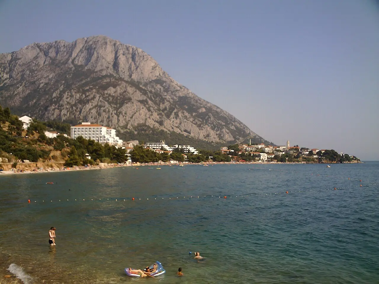 A Makarska Riviera beach resort with hotels and a village church below the steep grey Biokovo massif