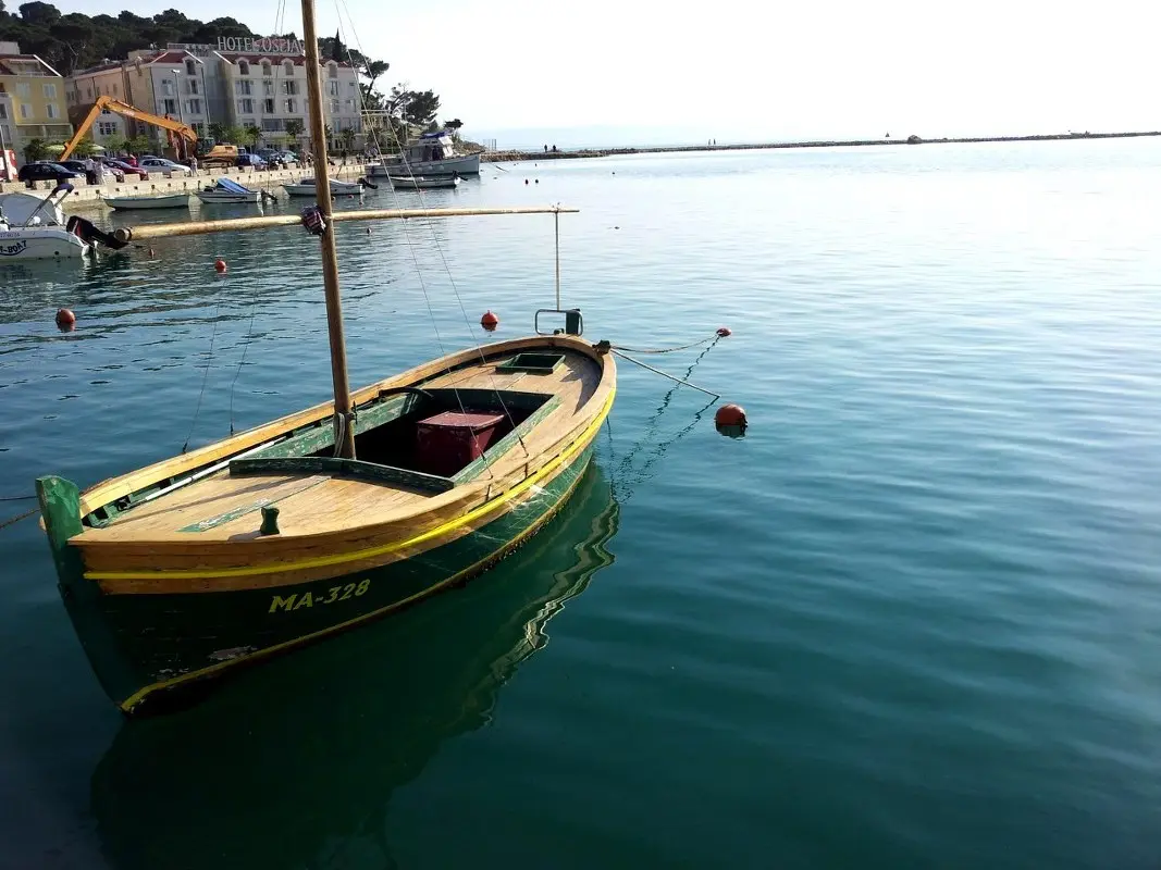 A traditional wooden fishing boat moored on the Makarska waterfront, with the town and a hotel behind