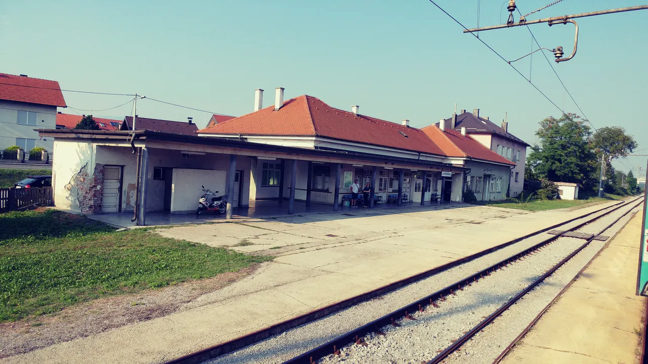 The single-storey station building and platform at Jastrebarsko under a clear sky, with the tracks running past