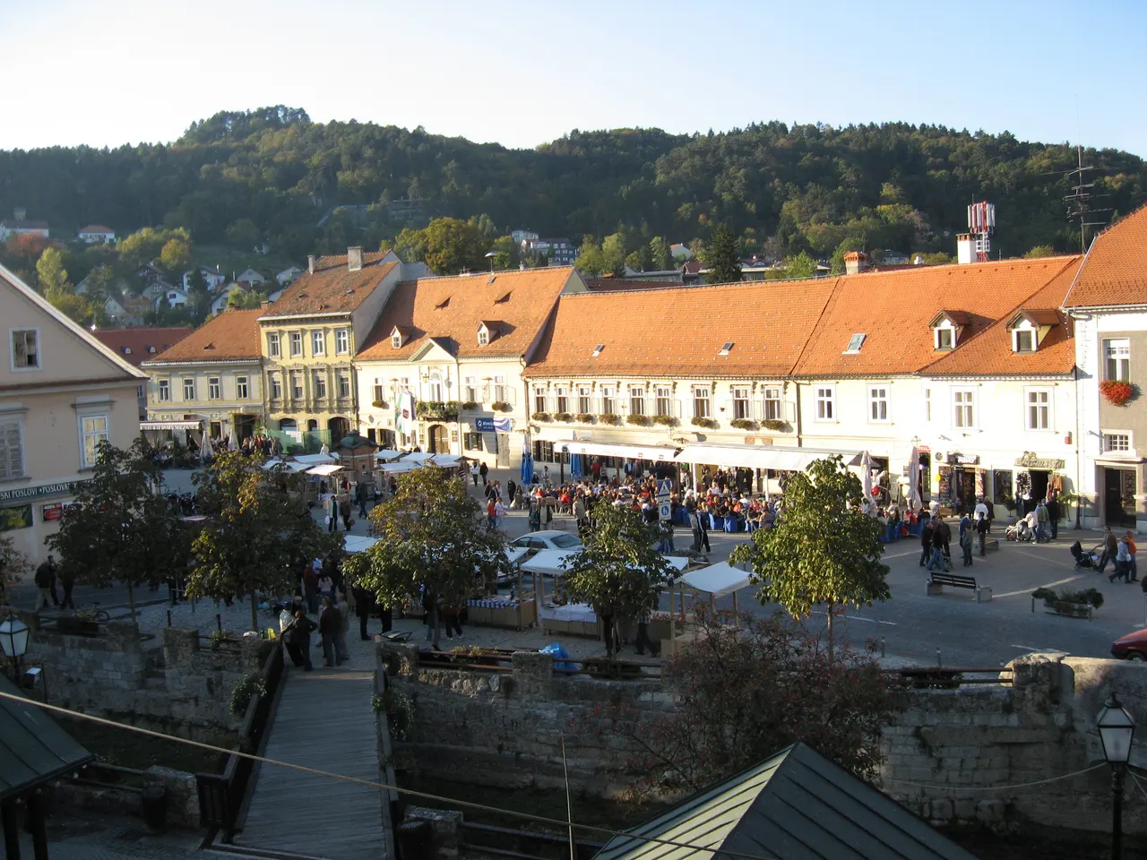 King Tomislav Square in Samobor with market stalls and café crowds in low autumn sun, wooded hills behind the town