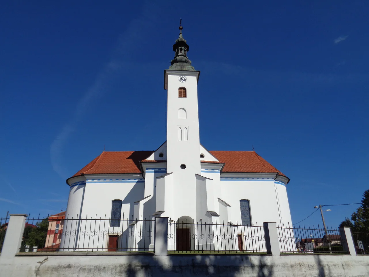 The white church of St Martin the Bishop with a tall bell tower and red roof in Sveti Martin na Muri under a deep blue sky