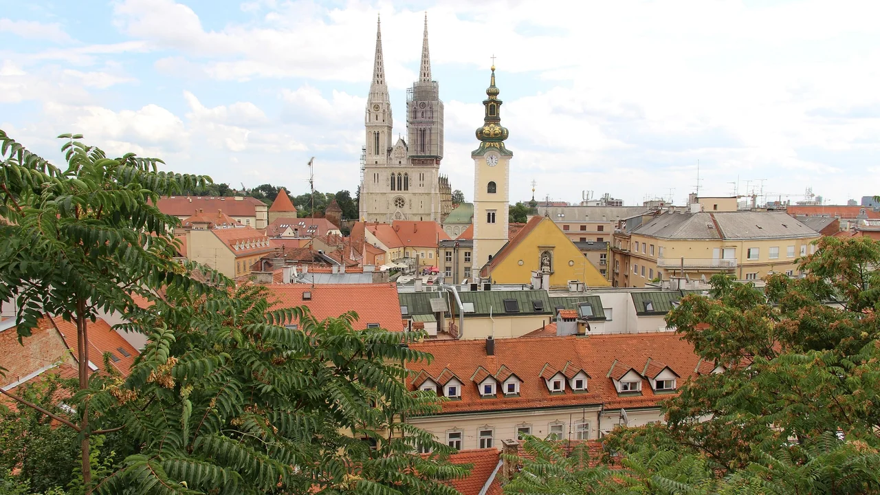 Red tiled roofs in central Zagreb with the two spires of the cathedral and a yellow clock tower with a green and gold dome above the treetops