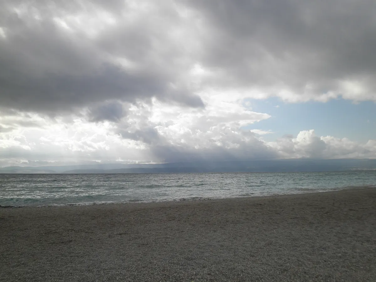 Omiš shoreline under a dramatic cloudy sky with the mountain ridge inland