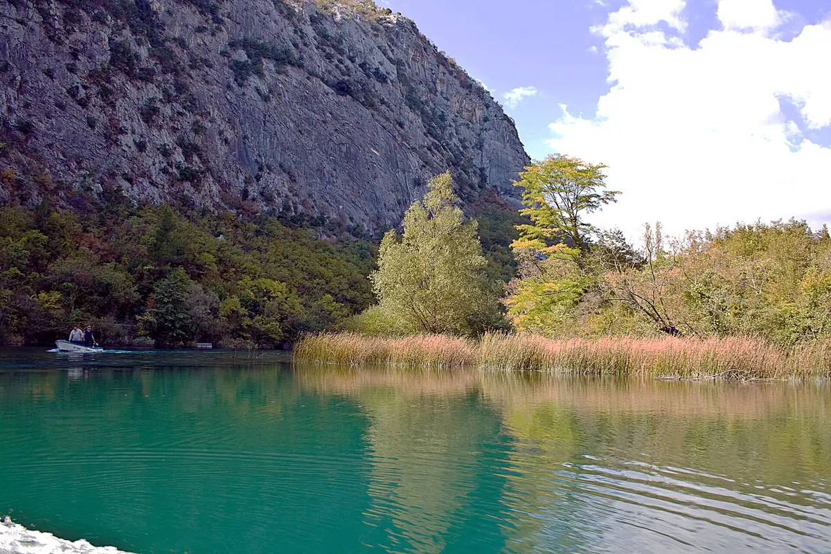 Small boat on the green Cetina river heading toward Omiš between canyon walls
