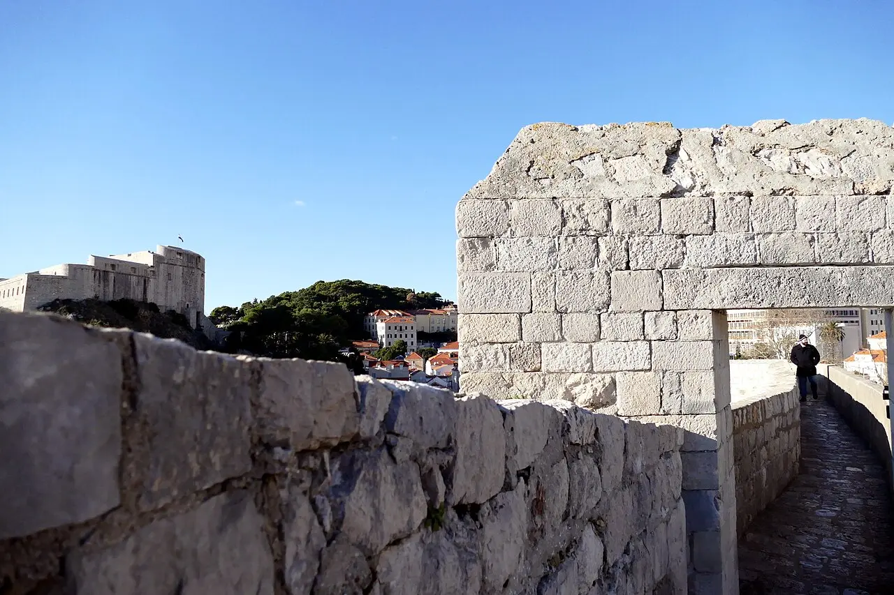 Visitors walking the stone rampart walkway of the Dubrovnik city walls above the Old Town rooftops