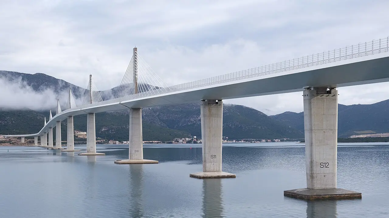 The Pelješac Bridge seen low over calm water, its concrete piers reflected and cable-stayed towers in mist