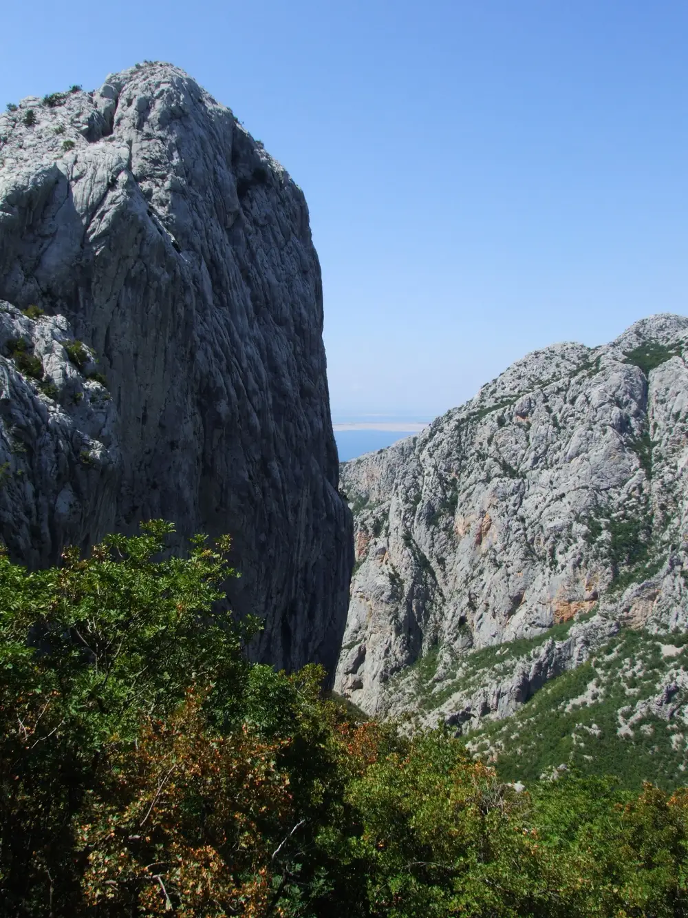 Looking through a narrow gap between two towering limestone cliffs in Velika Paklenica canyon, with the sea visible in the distance