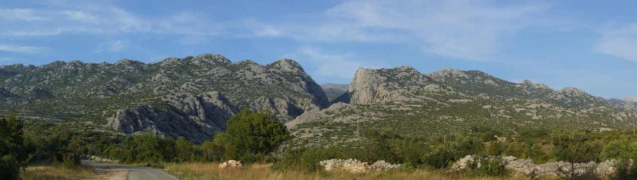 A wide view of the Velebit ridge from a country road, showing the narrow notch where Mala Paklenica canyon cuts through the mountains