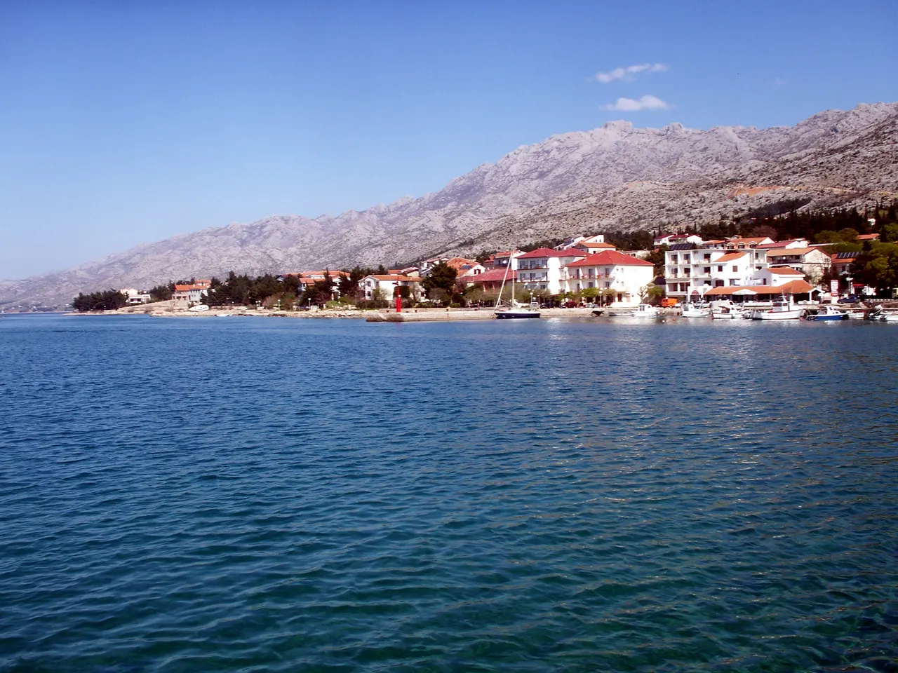 The small harbour and seafront of Starigrad-Paklenica with sailing boats moored and the Velebit mountains rising directly behind the town