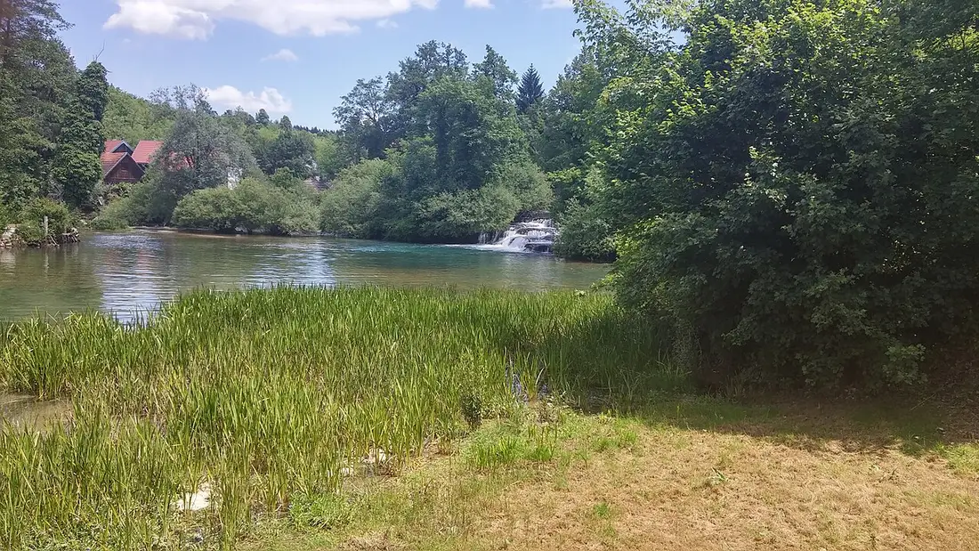 River with small cascades and a red-roofed house among greenery at Rastoke