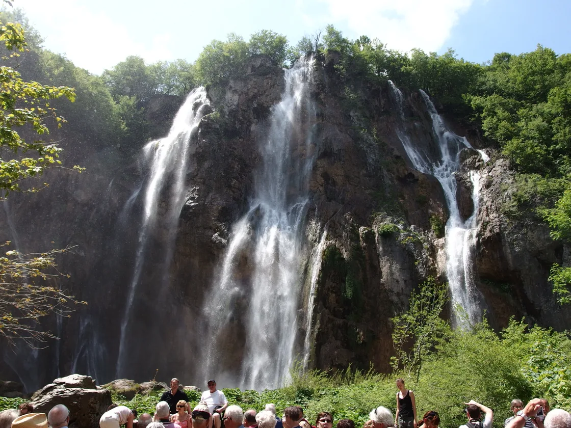 A dense crowd of visitors gathered at the base of the Veliki Slap waterfall at Plitvice
