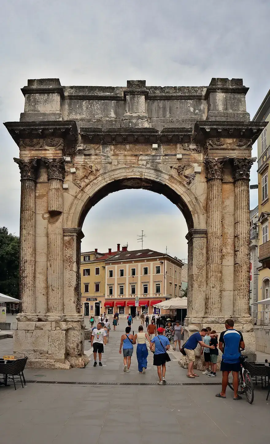 The Roman triumphal Arch of the Sergii in Pula, with people walking through it into the old town