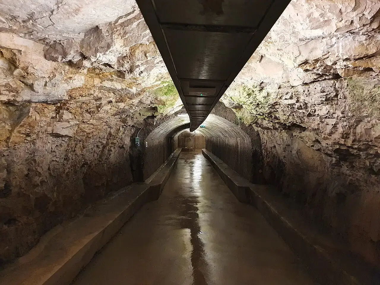 A vaulted underground passage of the Zerostrasse tunnels beneath Pula, lit dimly with a wet stone floor