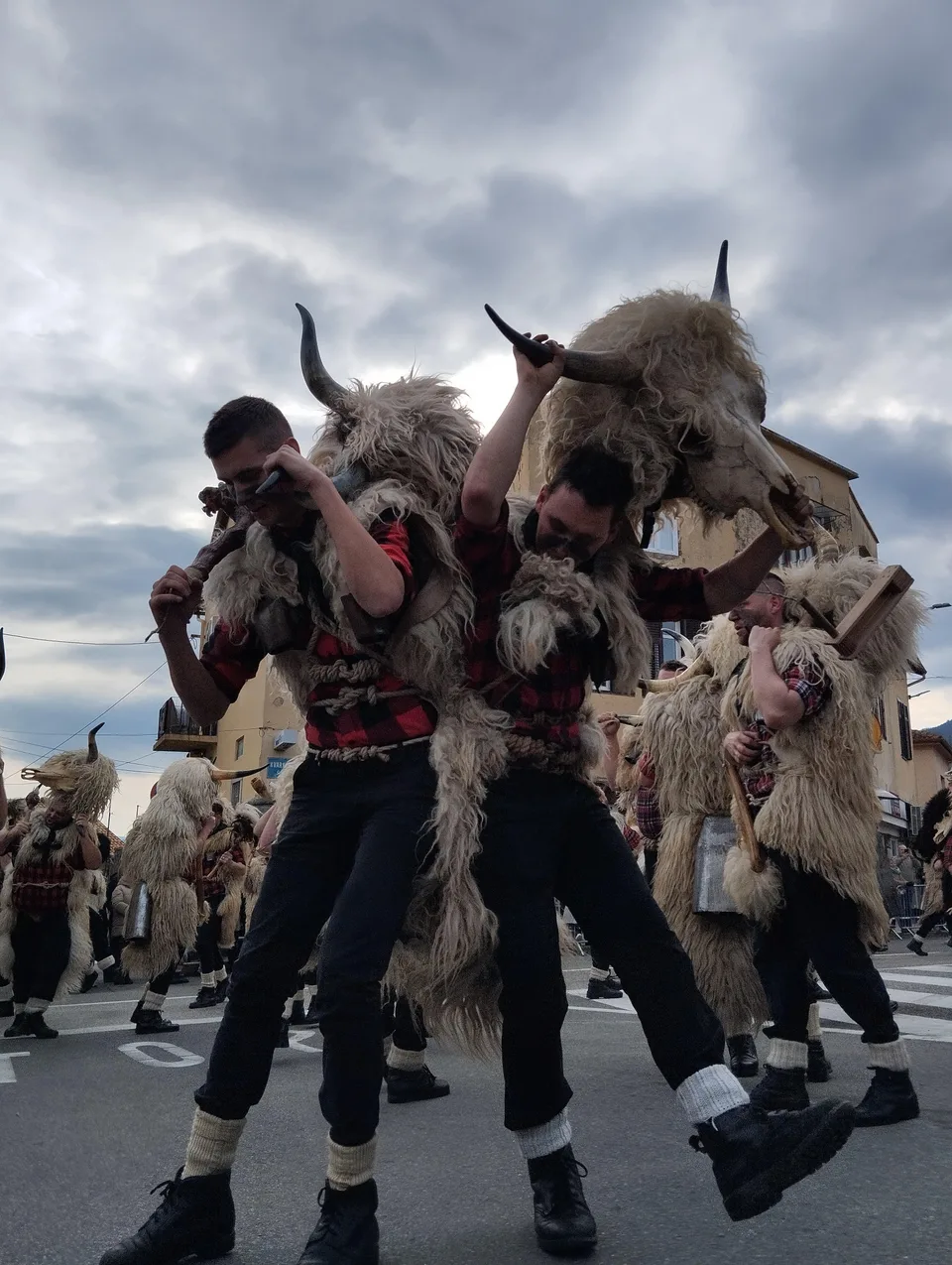 Bell ringers in shaggy sheepskins and horned animal masks marching down a Rijeka street with spectators behind them